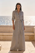 Woman wearing the Cala navy and cream striped cotton maxi shirt dress belted at the waist on a coastal terrace