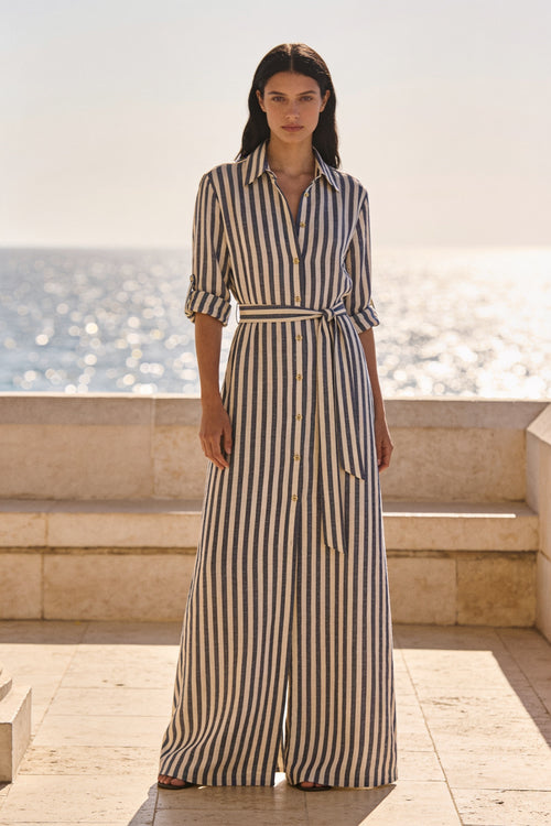 Woman wearing the Cala navy and cream striped cotton maxi shirt dress belted at the waist on a coastal terrace